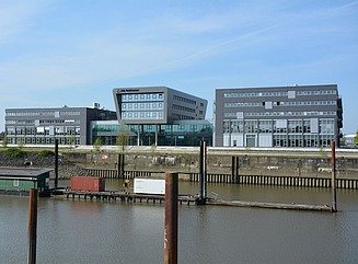 Weiße Industriehalle, mehrere Personen in Arbeitiskleidung, auf dem Boden Flugzeugteile, auf einer Wand der Aufdruck Airbus