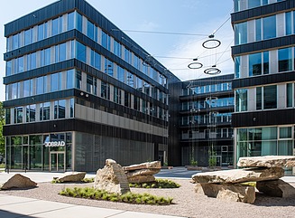 Corner building with horizontal window design, black cladding, construction fence in front of the building with the inscription Milestone