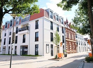 Weißes Eckgebäude mit hohen schmalen Fenstern, angrenzend an ein Gründerzeitgebäude mit heller, ziegelrot abgesetzter Fassade