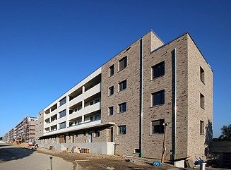 Boligkompleks med lyse rektangulære huse, altaner med mørkerødt rækværk