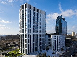 Hochhaus auf einem Platz, dahinter ein weiterer Bau mit 8 Geschossen, darüber eine halbkreisförmig gewölbte Fensterfassade