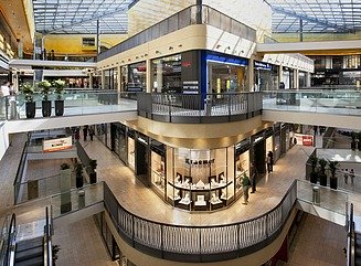 Abendlich beleuchtetes Gebäude im klassizistischen Stil mit Ladenschäften im Erdgeschoss ind hohen Säulen vor den zurückspringenden drei Geschossen